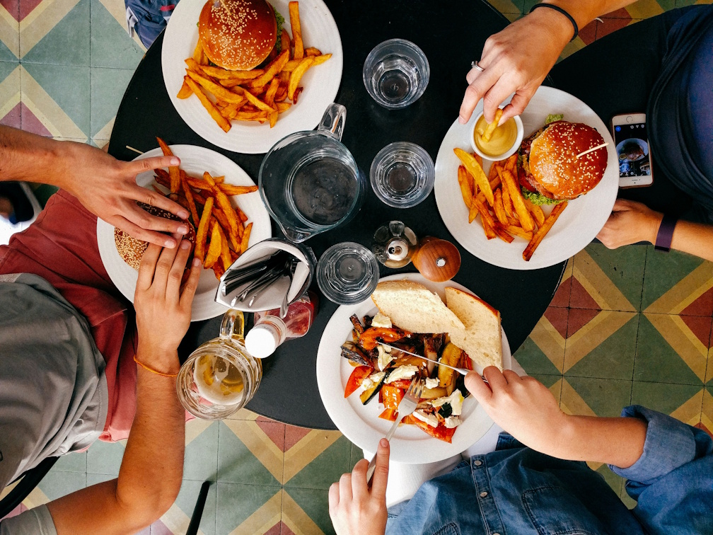 A table in a restaurant with people's hands reaching in for their meal.