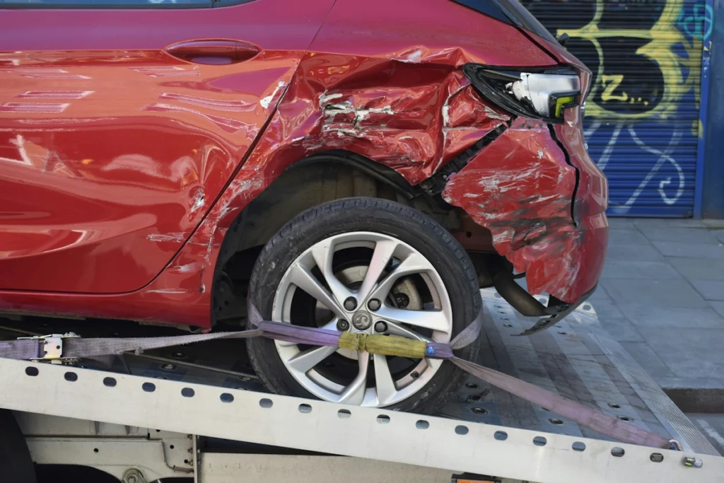 A badly damaged car on the back of a pick-up truck.